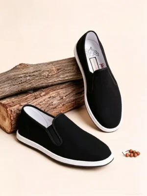 Angled side view of LUNO LN-M4011 men's black slip-on cloth shoes - casual style with elastic gusset and natural wood background
