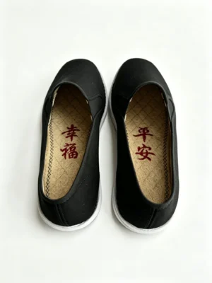 LUNO LN-M4023 men's cloth shoes top-down view - showcasing a pair of black canvas slip-ons with white rubber soles; the interior features textured natural loofah insoles embroidered with red Chinese characters "幸福" (Happiness) on the left and "平安" (Peace/Safety) on the right, highlighting breathable comfort and auspicious cultural symbolism.
